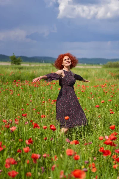 Haşhaş Tarlasında Çiçek Desenli Bir Elbise Giyen Kıvırcık Saçlı Kızıl — Stok fotoğraf