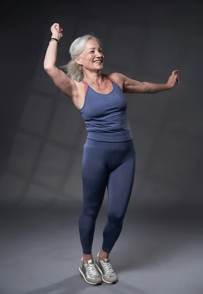 白发苍苍的老年妇女正在上健身课 背景是灰色的 — 图库照片