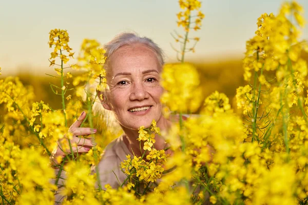 美しいですシニア女性白い髪で菜の花畑 — ストック写真