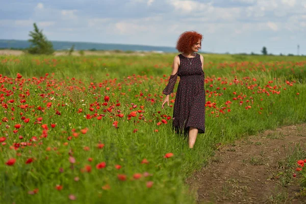 罂粟田里穿着花衣的卷发红头发妇女 — 图库照片