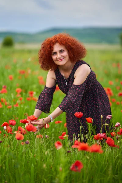 Haşhaş Tarlasında Çiçek Desenli Bir Elbise Giyen Kıvırcık Saçlı Kızıl — Stok fotoğraf