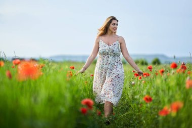 Haşhaş tarlasında çiçek desenli elbiseler giyen güzel, iri yarı Hintli bir kadın.