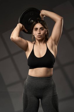 Güçlü beden ölçüleri ve gri arka planda ağırlık çalışan Hintli kadın.