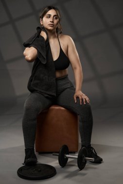 Güçlü beden ölçüleri ve gri arka planda ağırlık çalışan Hintli kadın.