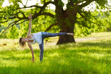 Yüzüncü yıl meşe ağaçlarıyla dolu bir ormanda yoga ve meditasyon yapan genç bir kadın.