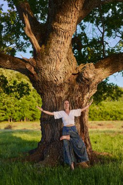 Yüzüncü yıl meşe ağaçlarıyla dolu bir ormanda yoga ve meditasyon yapan genç bir kadın.