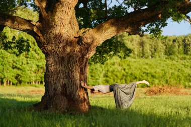 Yüzüncü yıl meşe ağaçlarıyla dolu bir ormanda yoga ve meditasyon yapan genç bir kadın.