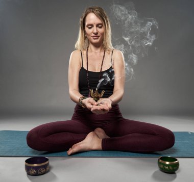Yoga yaparken elinde yanık kokulu tütsü tutan genç bir kadın.