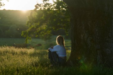 Gün batımında kocaman bir meşe ağacının yanında poz veren çekici sarışın kadın.