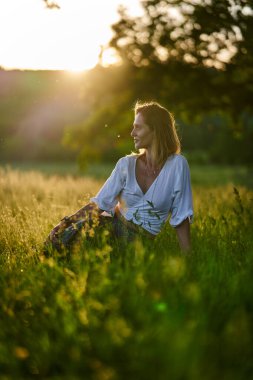 Gün batımında kocaman bir meşe ağacının yanında poz veren çekici sarışın kadın.