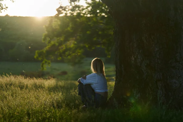 Gün batımında kocaman bir meşe ağacının yanında poz veren çekici sarışın kadın.
