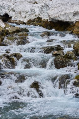 Dağ nehri ve yaz başında karlı dağlık araziler.
