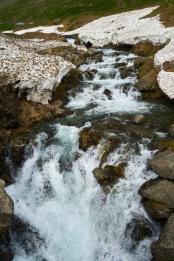 Dağ nehri ve yaz başında karlı dağlık araziler.