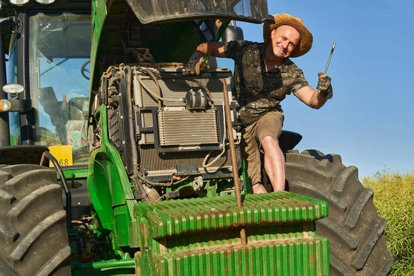 彼の壊れたトラクターを修理しようとしている農業機械工は カノーラフィールドの真ん中に — ストック写真