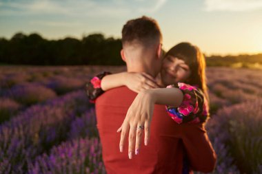 Genç mutlu çift gün batımında lavanta tarlasında nişan yüzüğünü gösteriyor.