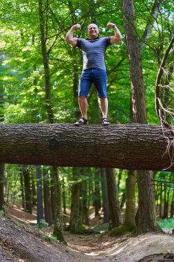 Strong athletic man climbing on a tree bark over a trail flexing his biceps