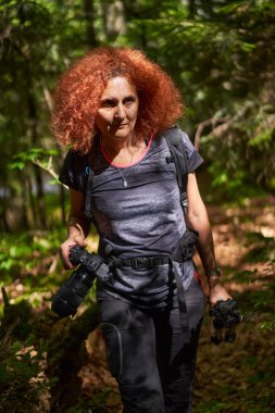 Nature photographer lady with camera and backpack hiking on a trail in the forest mountain