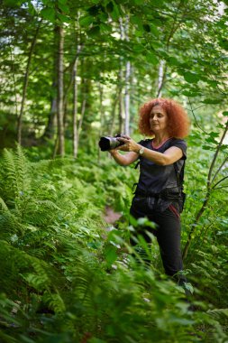 Nature photographer lady with camera and backpack hiking on a trail in the forest mountain