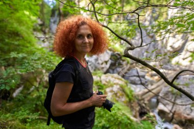 Nature photographer lady with camera and backpack hiking on a trail in the forest mountain
