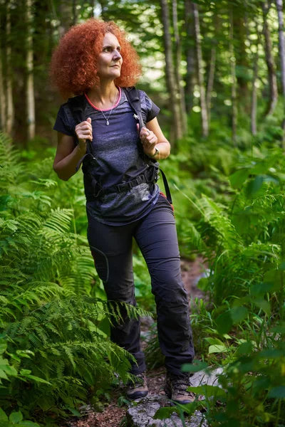 Woman hiker with backpack hiking on a trail in the mountain forest