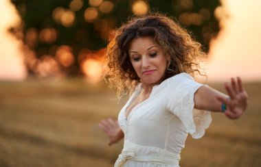 Curly haired caucasian woman in a harvested wheat field at sunset, portrait with selective focus