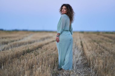Curly haired caucasian woman in a harvested wheat field at sunset, portrait with selective focus