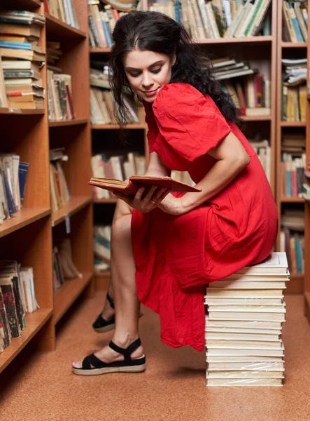 Красива Жінка Червоній Сукні Бібліотеці Сидить Стопі Книг Читаючи — стокове фото