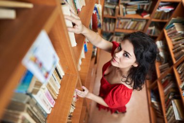 Attractive brunette librarian in red dress in a library full of books