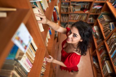 Attractive brunette librarian in red dress in a library full of books