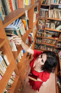 Attractive brunette librarian in red dress in a library full of books
