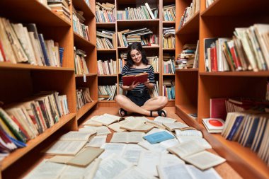 Attractive young woman in striped top and black mini skirt in a library full of books, posing as a librarian or student