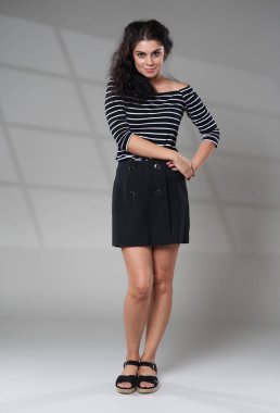 Beautiful cheerful young brunette woman in black skirt and striped top, studio shot with window projection in background
