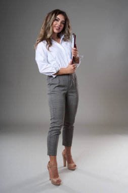 Dosyasıyla ve belgeleriyle genç ve çekici bir iş kadınının tam boy portresi, gri arka planda bir stüdyo resmi.