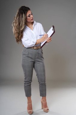 Dosyasıyla ve belgeleriyle genç ve çekici bir iş kadınının tam boy portresi, gri arka planda bir stüdyo resmi.