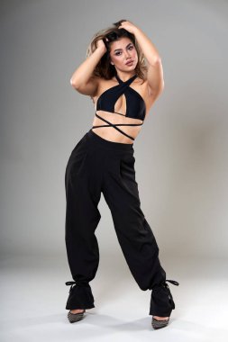 Gri arka planda siyah bluzlu ve pantolon stüdyosunda çekilen güzel, modaya uygun genç bir model.