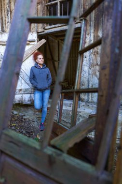 Kıvırcık saçlı, ekose gömlekli ve kot pantolonlu bir kadın harap bir ahırda ve evde.