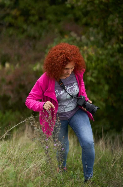 写真家の赤毛巻き毛の女性は彼女のカメラで森の中でハイキング — ストック写真