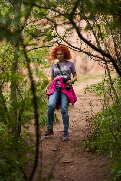 Fotoğrafçı Kızıl Saçlı Kıvırcık Saçlı Kadın Kamerasıyla Ormanda Yürüyüş Yapıyor — Stok fotoğraf