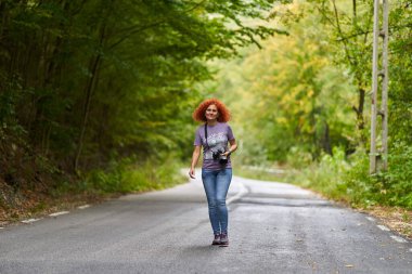 Turist, kızıl, kıvırcık saçlı, ormanda dağ yolunda kameralı kadın.