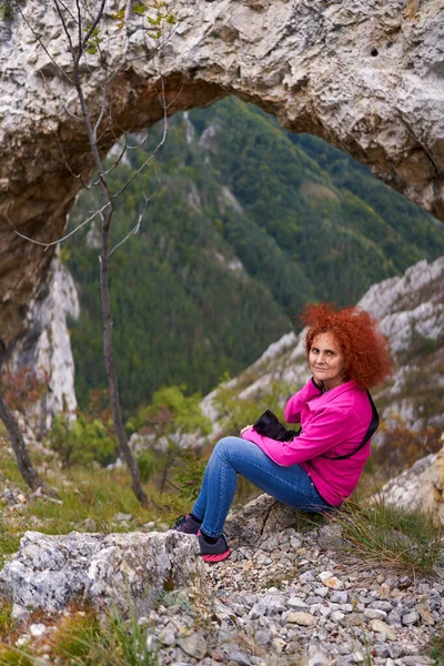 山の中の天然の岩のポータルで休んでカメラを持つ女性ハイカー — ストック写真