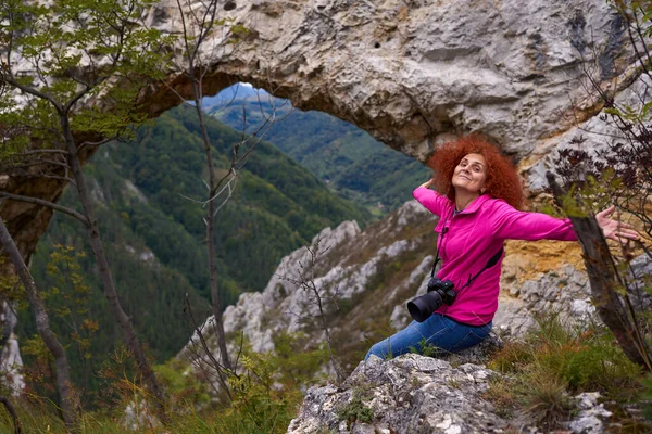 Kameralı Bir Kadın Yürüyüşçü Dağlarda Doğal Bir Kaya Portalının Yanında — Stok fotoğraf