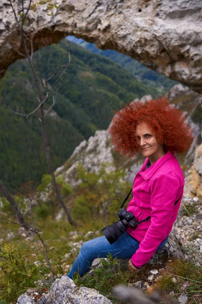 女徒步旅行者 带着相机 在山中的天然岩石门边歇息 — 图库照片