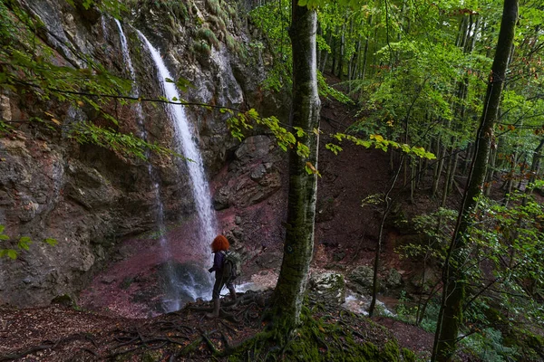 山の中の滝でバックパックとカメラのハイキングを持つ女性の自然写真家 — ストック写真