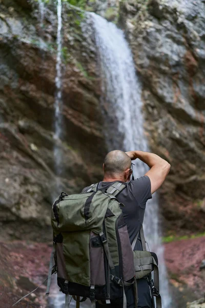 山の森の滝でカメラとバックパック付きのプロの自然写真家 — ストック写真