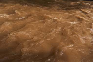 Nehir çamurlu sularla dolup taşar, dalgalar ve akıntılar yaratır.