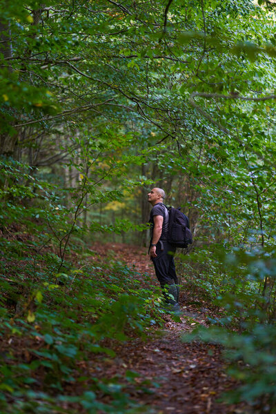 Experienced hiker making his way through an old lush forest on a hiking trail