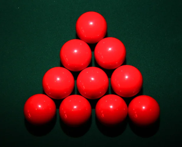 A set of red snooker balls in a triangle on green pool table