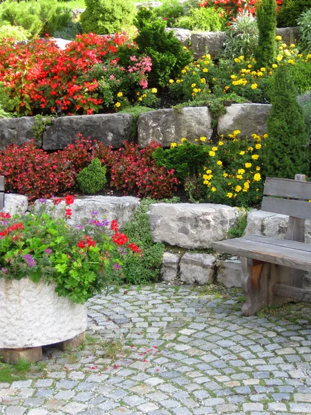 Stone wall, bench and plants on colorful landscaped garden. — Stock Photo, Image