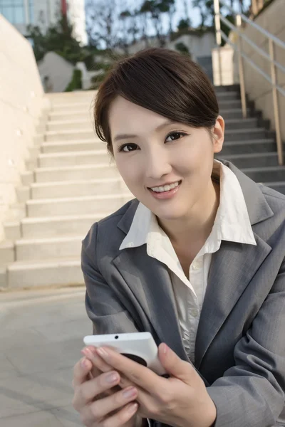 Sorridente asiatica donna d'affari utilizzando il cellulare e sedersi sulle scale a — Foto Stock