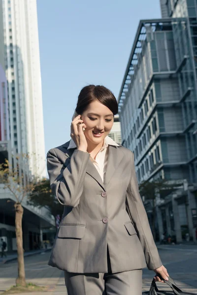 Felice donna d'affari asiatica parlando al telefono e camminando su stree — Foto Stock